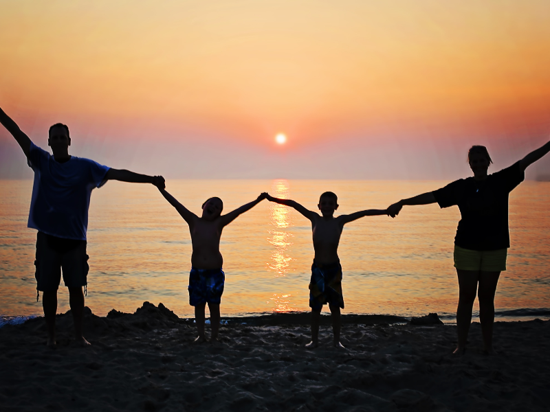 Family holding hands in silhouette at sunset