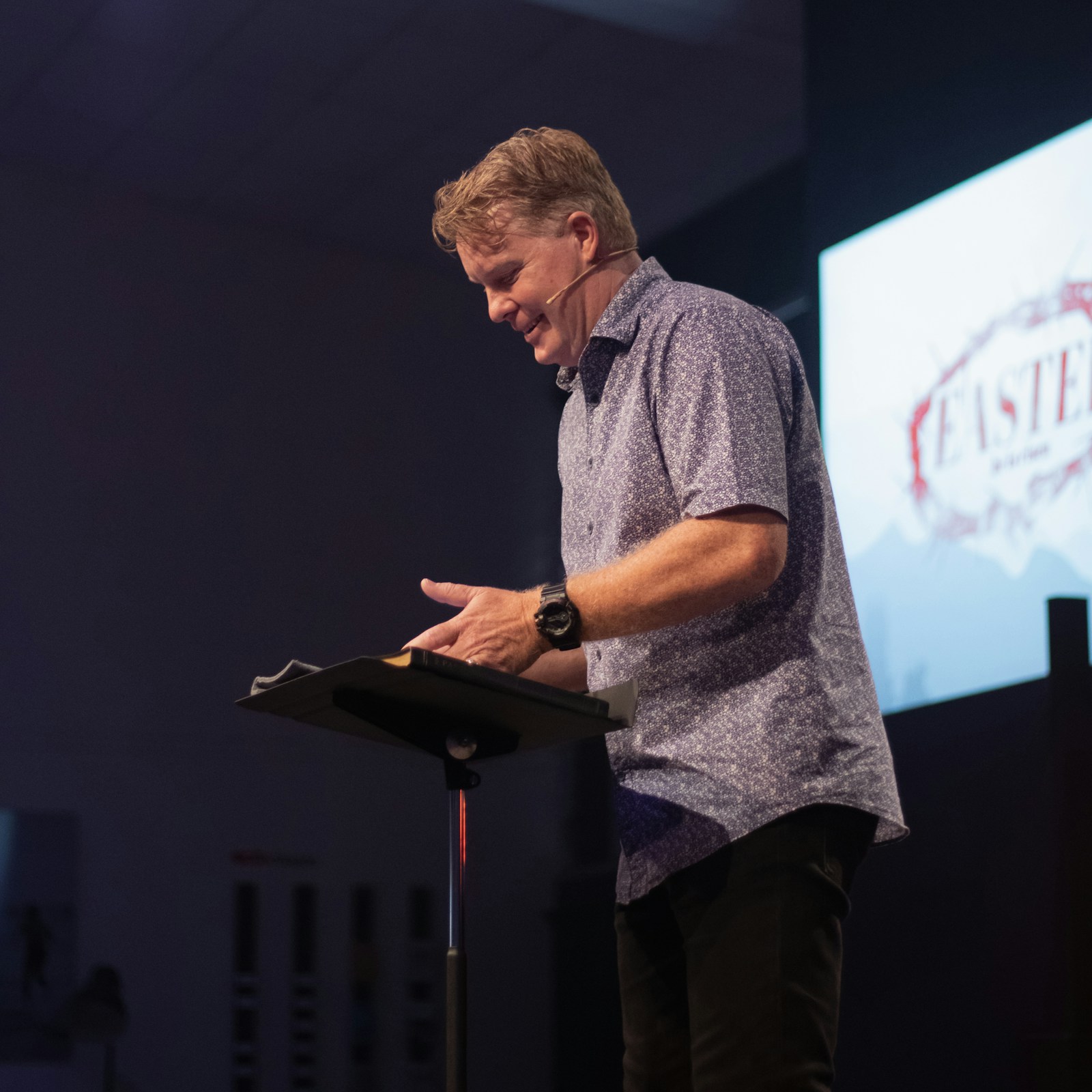 Male pastor in everyday attire preaching with an open Bible